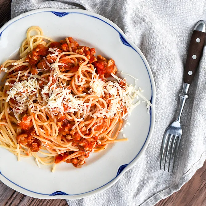 Broileribolognese lautasella, jossa on sininen reunus.