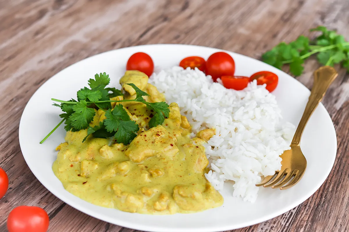 Curry-kanakastiketta lautasella riisin ja tuoreen korianterin kanssa.