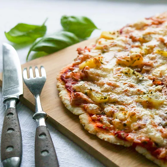 Gluteenittomalla pizzapohjalla leivottu pizza, jonka rinnalla on rouhea haarukka ja veitsi.