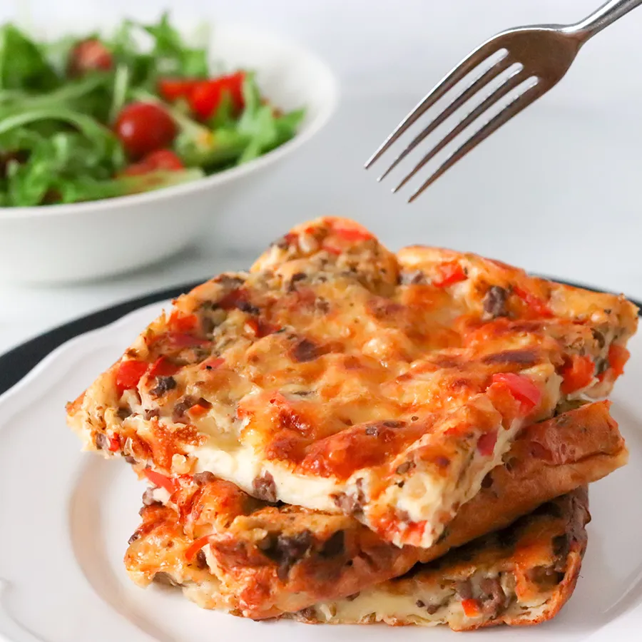 Jauhelihapannukakkua lautasella, jonka takana on salaattia.