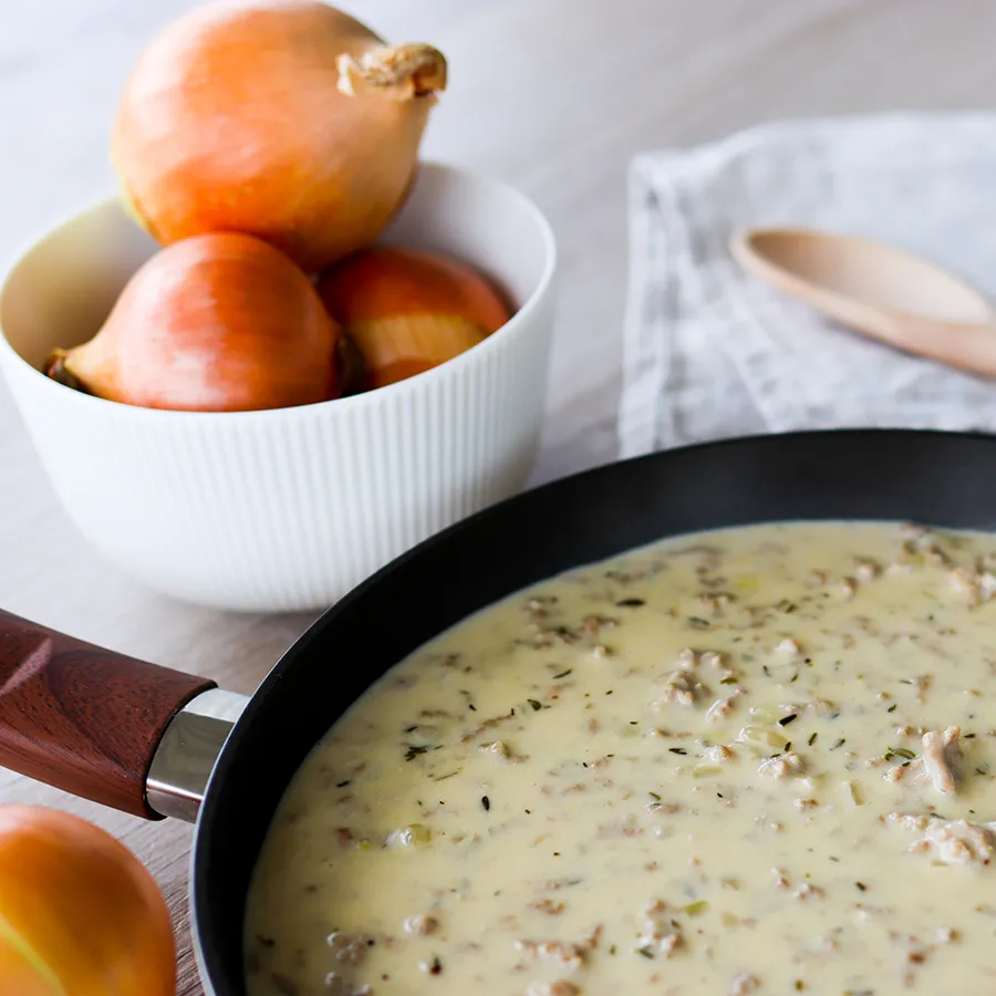 Kermainen jauhelihakastike pannulla, jonka taustalla on keltasipuleita.