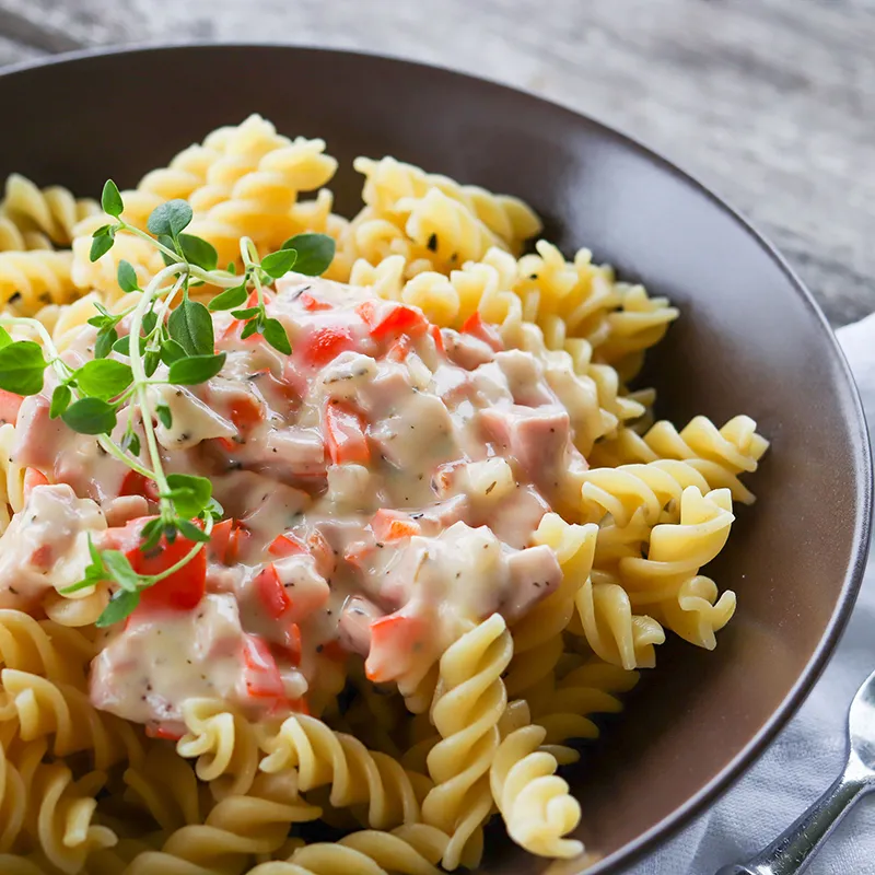 Kinkkukastike ja kierrepastaa ruskealla lautasella.