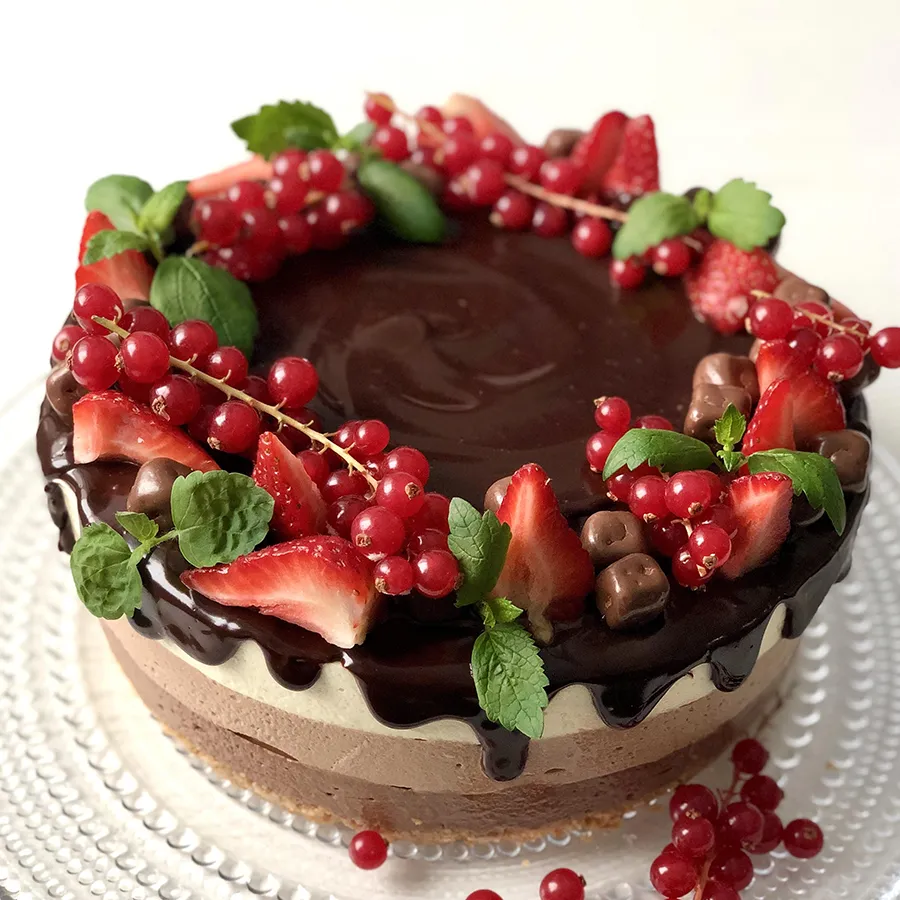 Kolmen suklaan juustokakku, jonka päällä on punaherukoita.