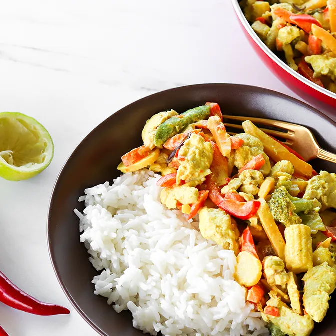 Kookoskana ruskealla lautasella riisin kera.