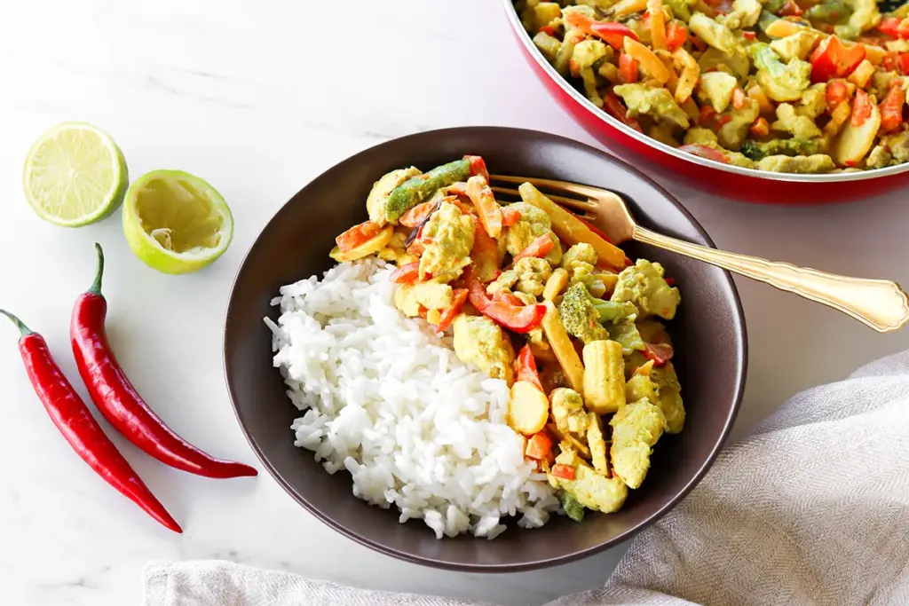 Kookoskana riisin kanssa lautasella sekä tuoretta chiliä ja limeä.