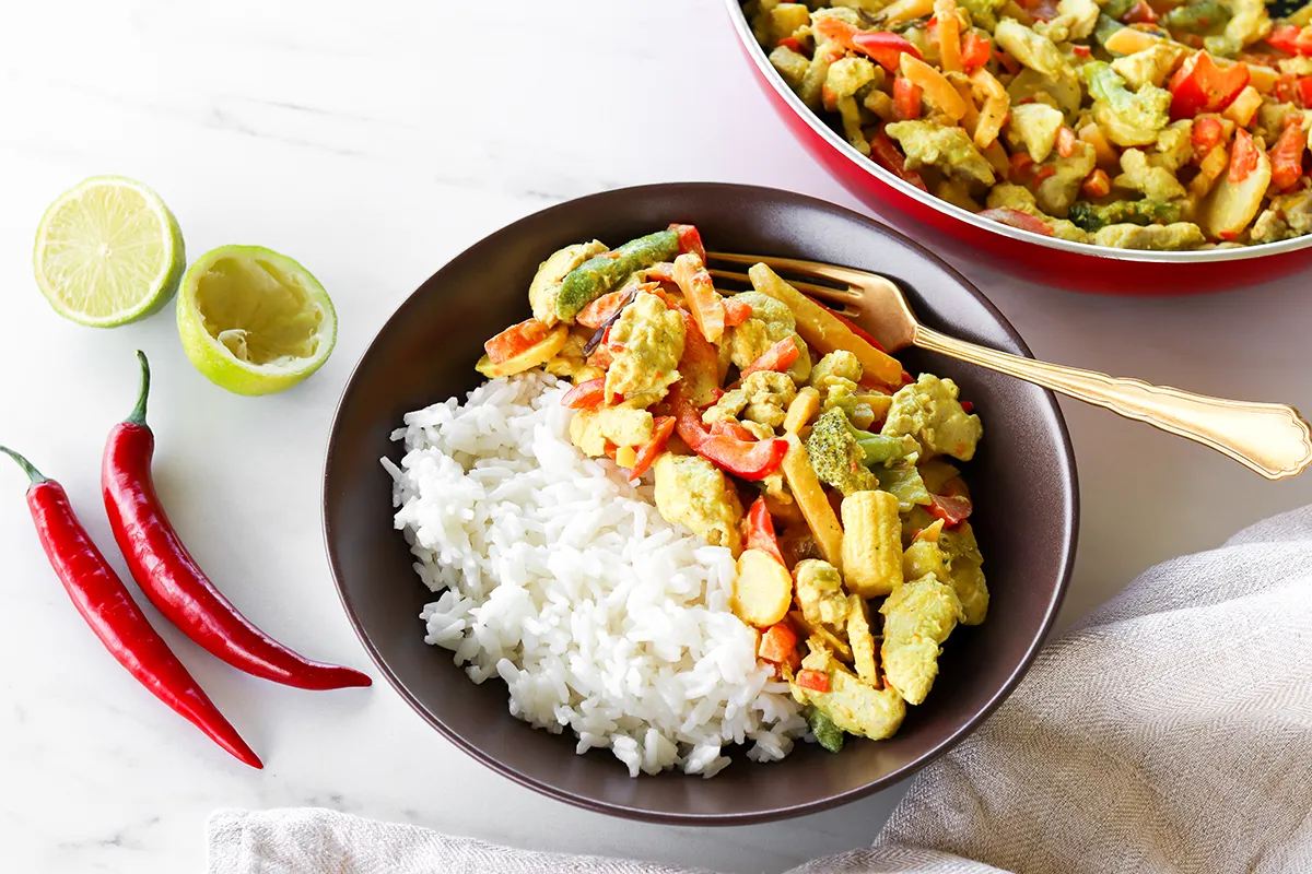 Kookoskana riisin kanssa lautasella sekä tuoretta chiliä ja limeä.