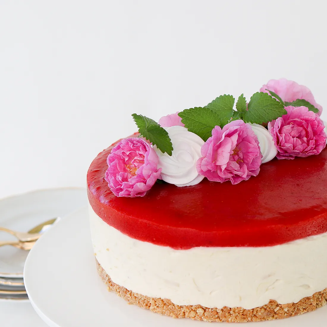 Mansikka-raparperijuustokakku, jonka päällä on vaaleanpunaisia ruusuja.