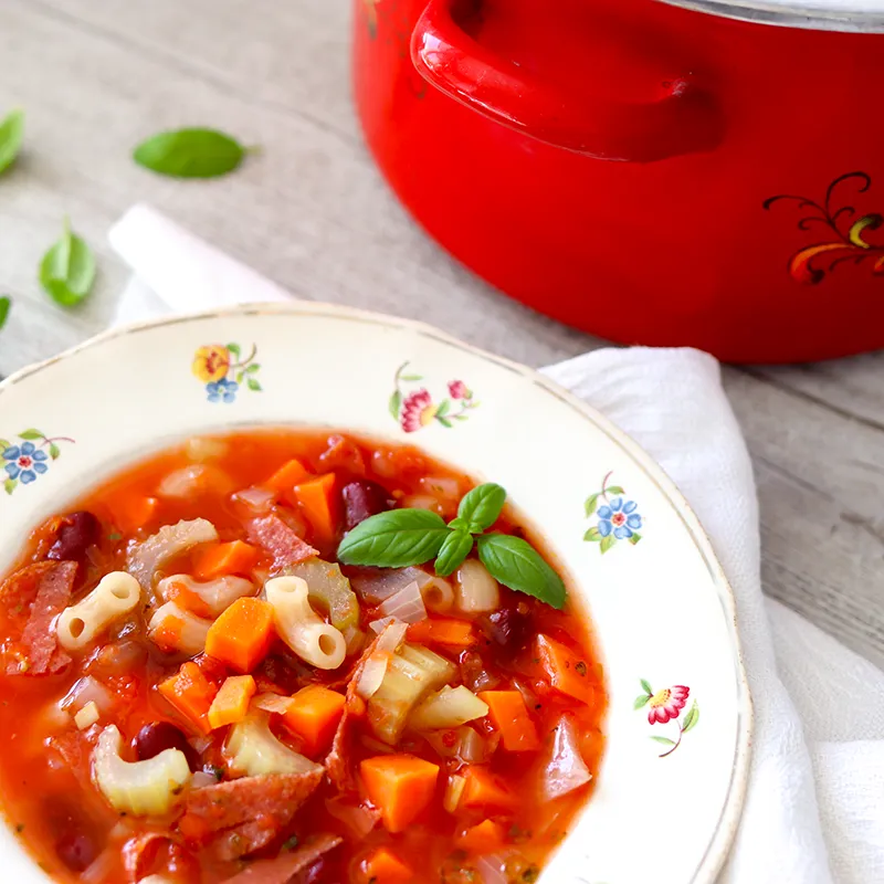 Minestronekeitto lautasella punaisen kattilan vierellä.