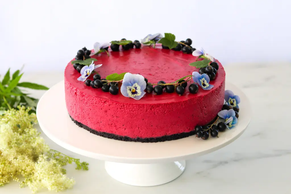 Tuoreilla marjoilla koristeltu mustaherukka-juustokakku jalallisen kakkulautasen päällä.