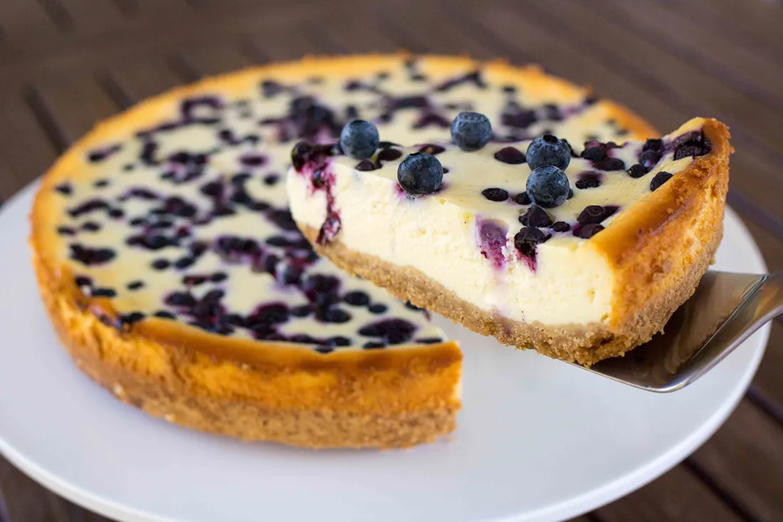 Mustikka-valkosuklaajuustokakku, josta on leikattu pala.