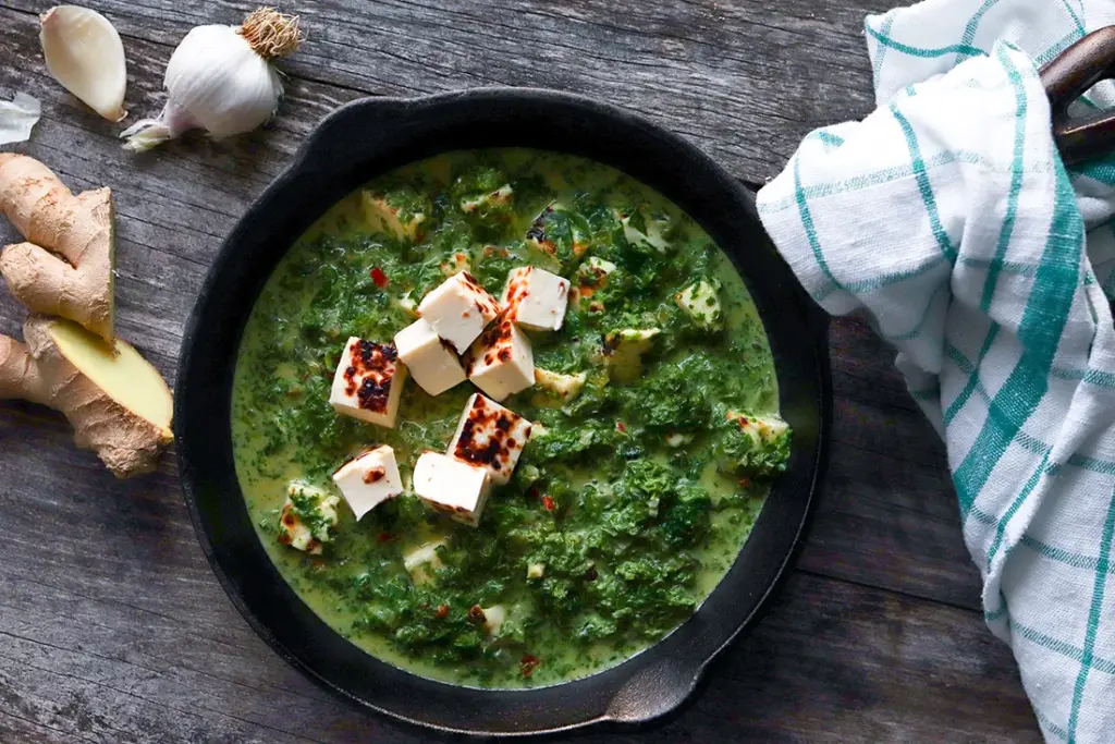 Palak paneer leipäjuustosta mustalla paistinpannulla.