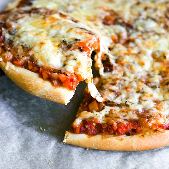 Pizzapohja kuivahiivalla tehtynä pyöreänä pizzana leivinpaperin päällä.