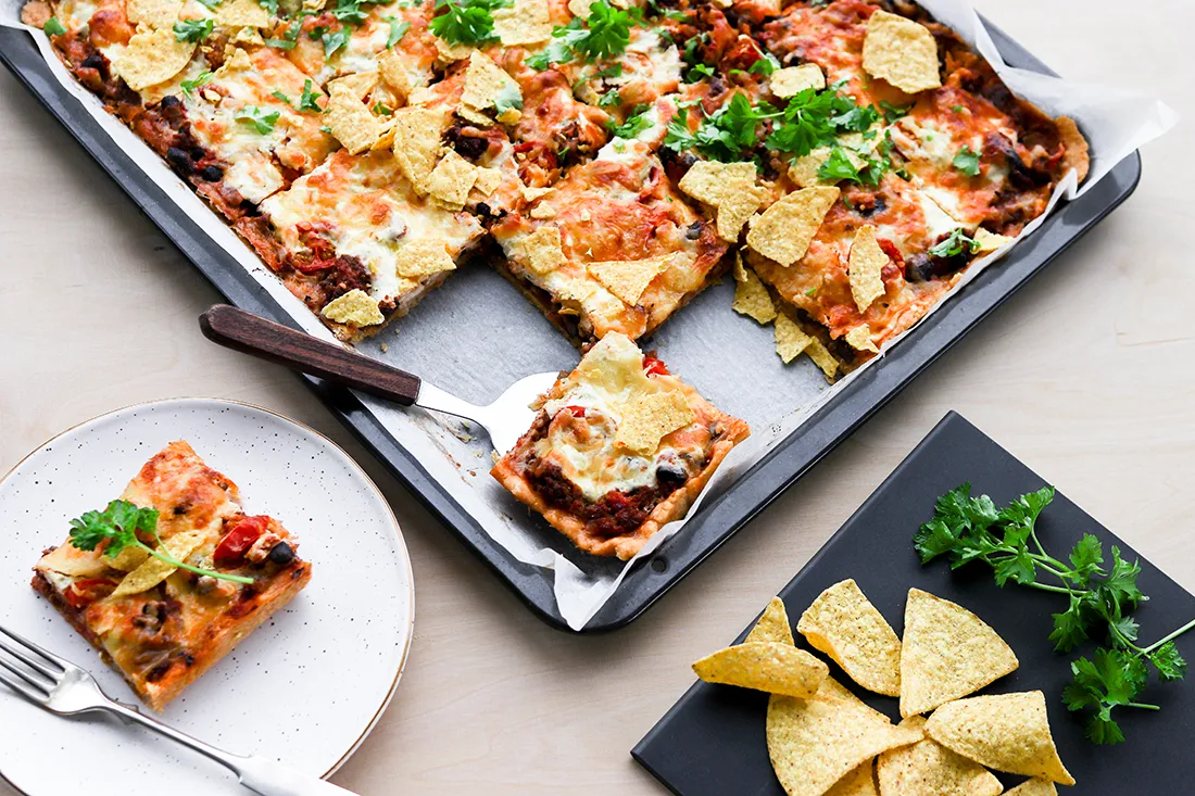 Jauheliha-tacopiirakka pellillä paloiksi leikattuna ja nachoilla koristeltuna