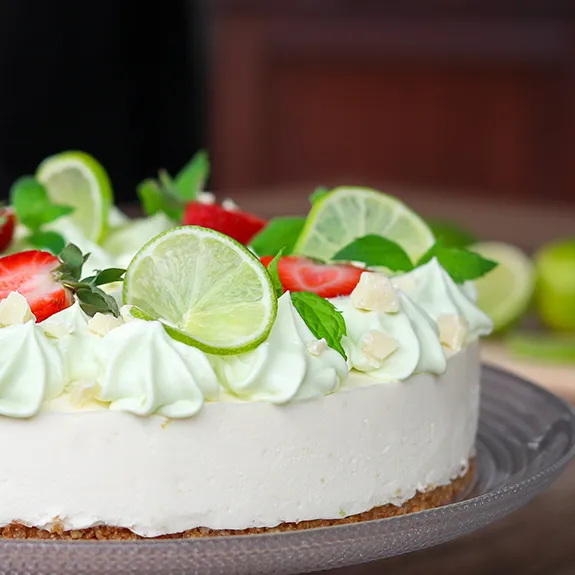 Valkosuklaa-limejuustokakku koristeltuna lasilautasen päällä.