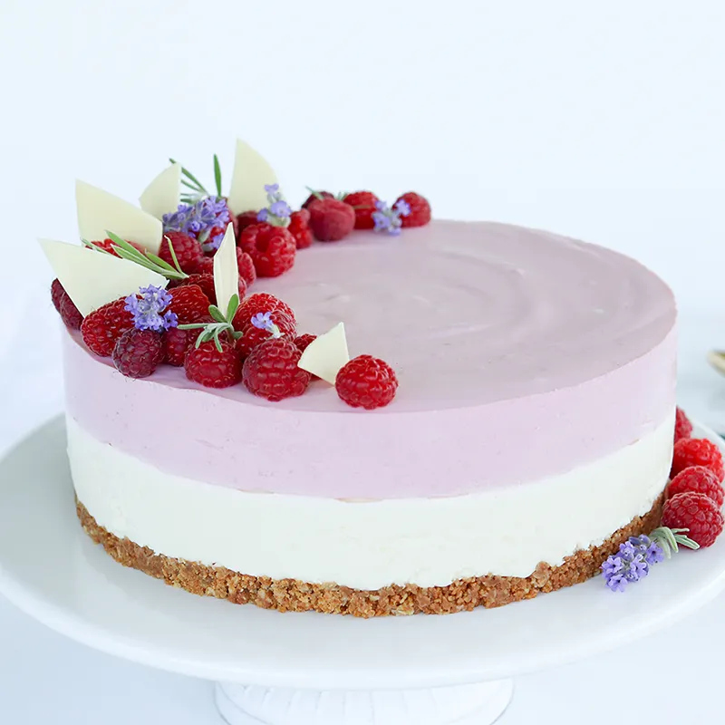 Valkosuklaa-vadelmajuustokakku, jonka päällä on marjoja, kukkia ja suklaakoristeita.