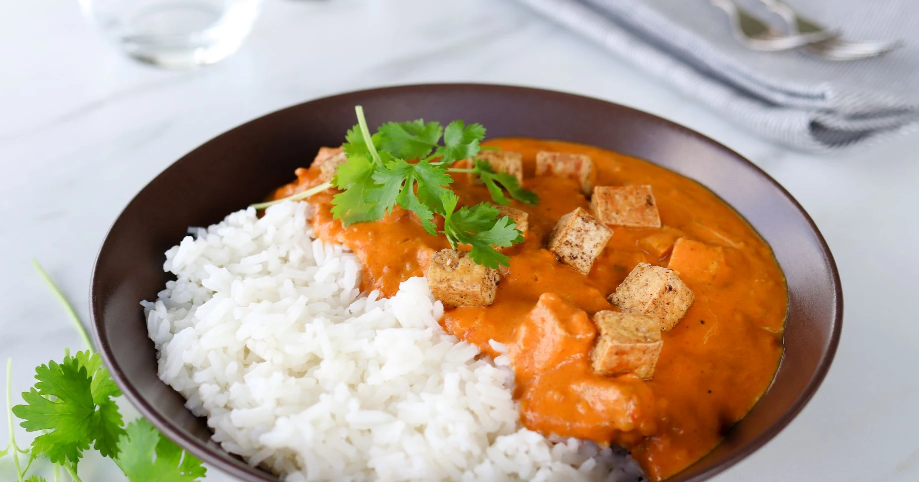 Butter tofu ruskealla lautasella riisin ja korianterin kera.