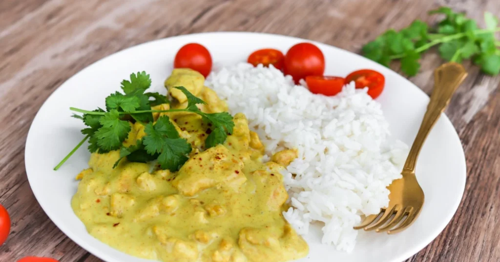 Curry-kanakastiketta lautasella riisin ja tuoreen korianterin kanssa.