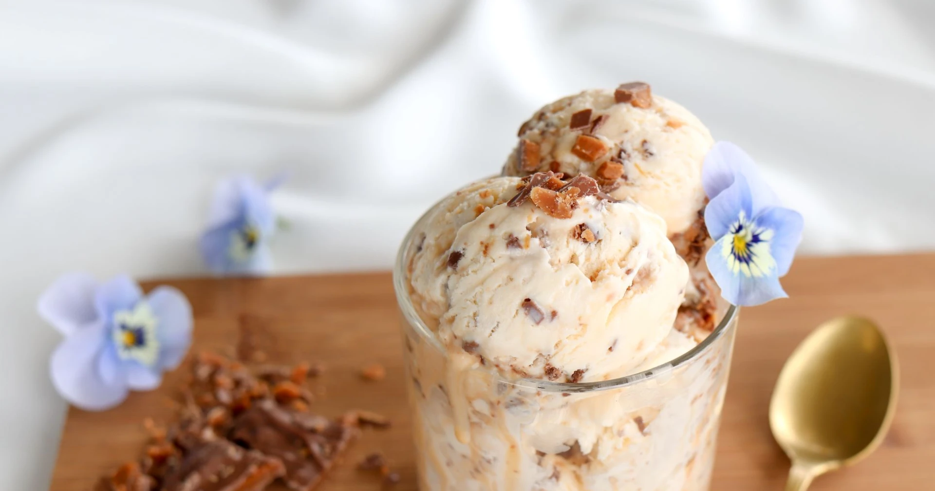 Itse tehty Daim-jäätelö sinisellä orvokilla koristeltuna lasissa.