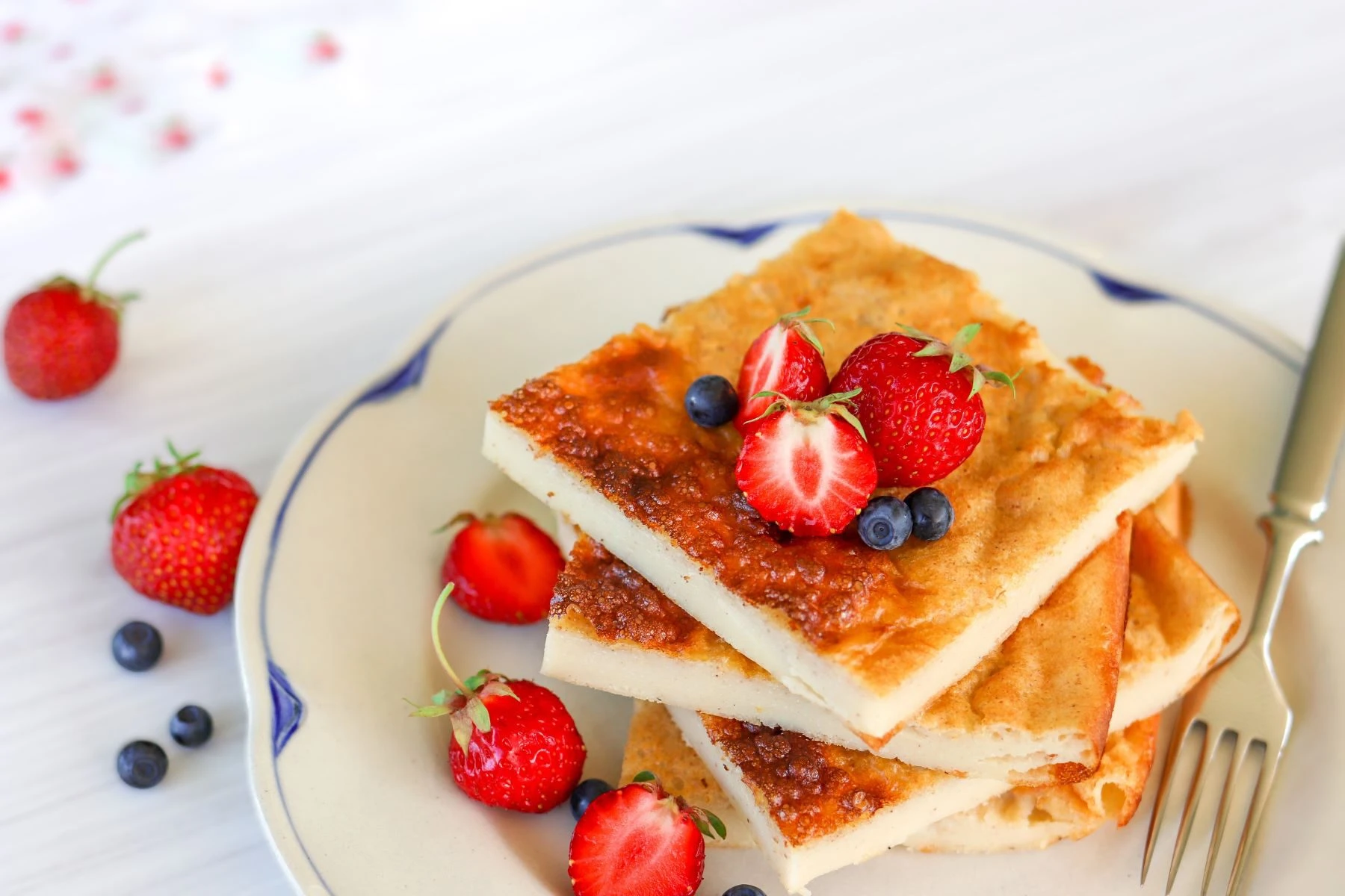 Gluteeniton pannukakku paloiksi leikattuna tuoreiden mansikoiden ja mustikoiden kanssa.