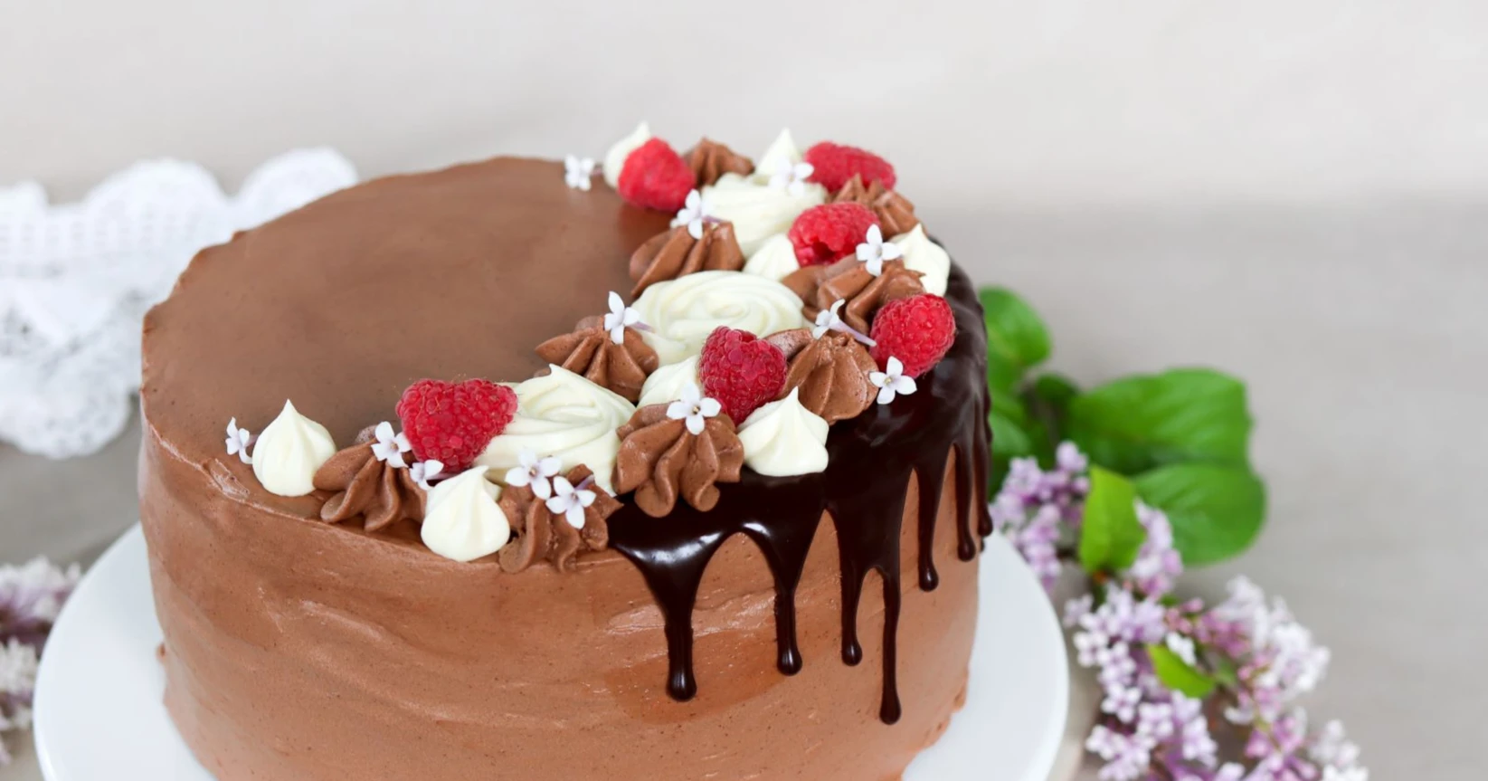 Gluteeniton suklaakakku suklaavalumilla, pursotuksilla ja vadelmilla koristeltuna.