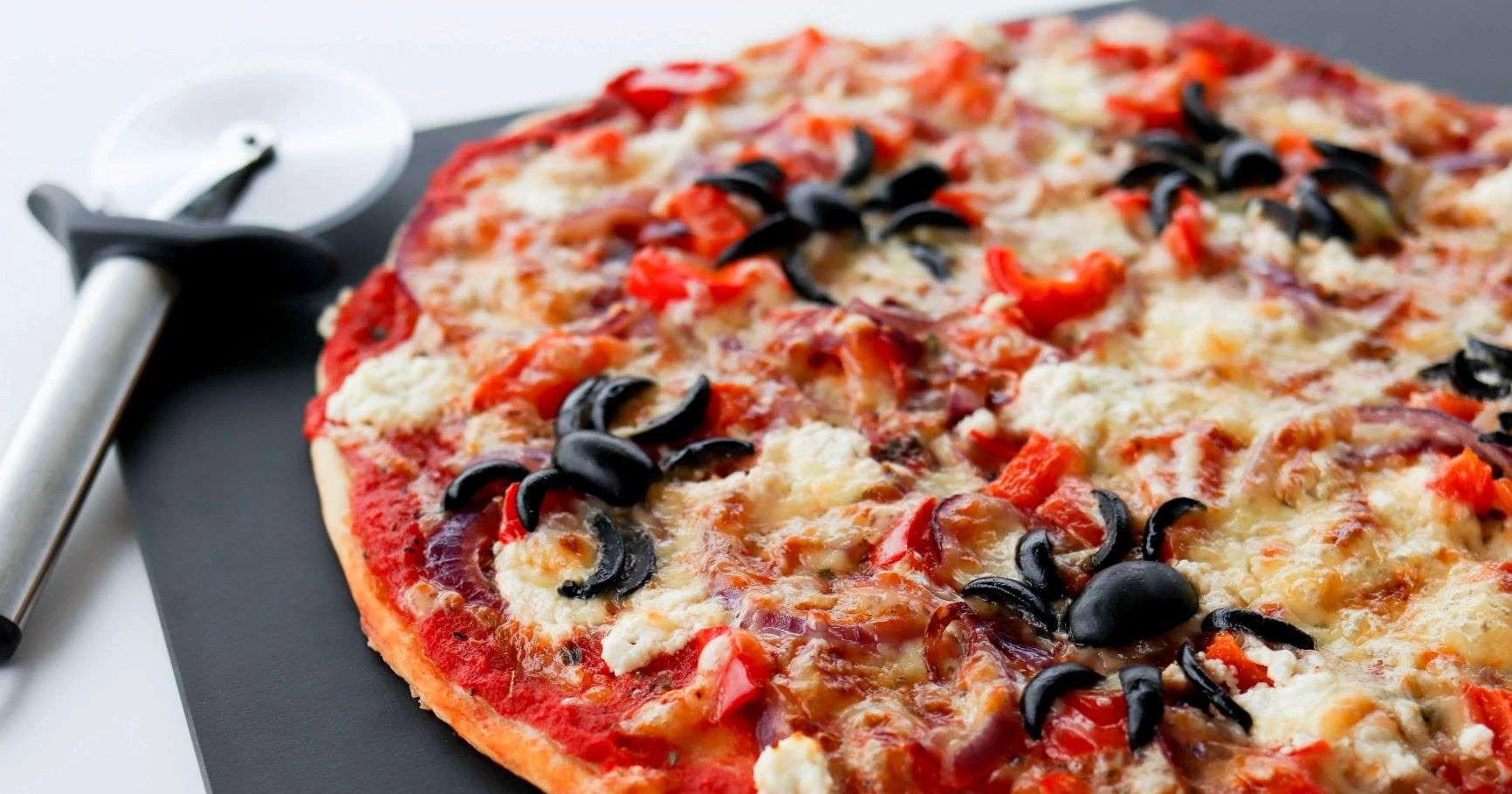 Pizza, jonka päällä on oliiveista tehtyjä hämähäkkejä.