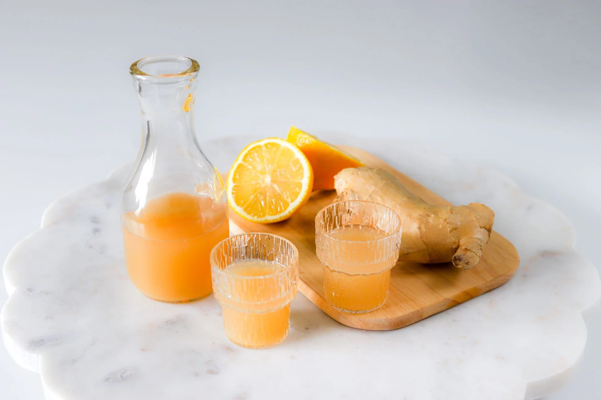 Inkiväärishotti pienessä lasissa, jonka vierellä on tuoretta sitruunaa ja inkivääriä.