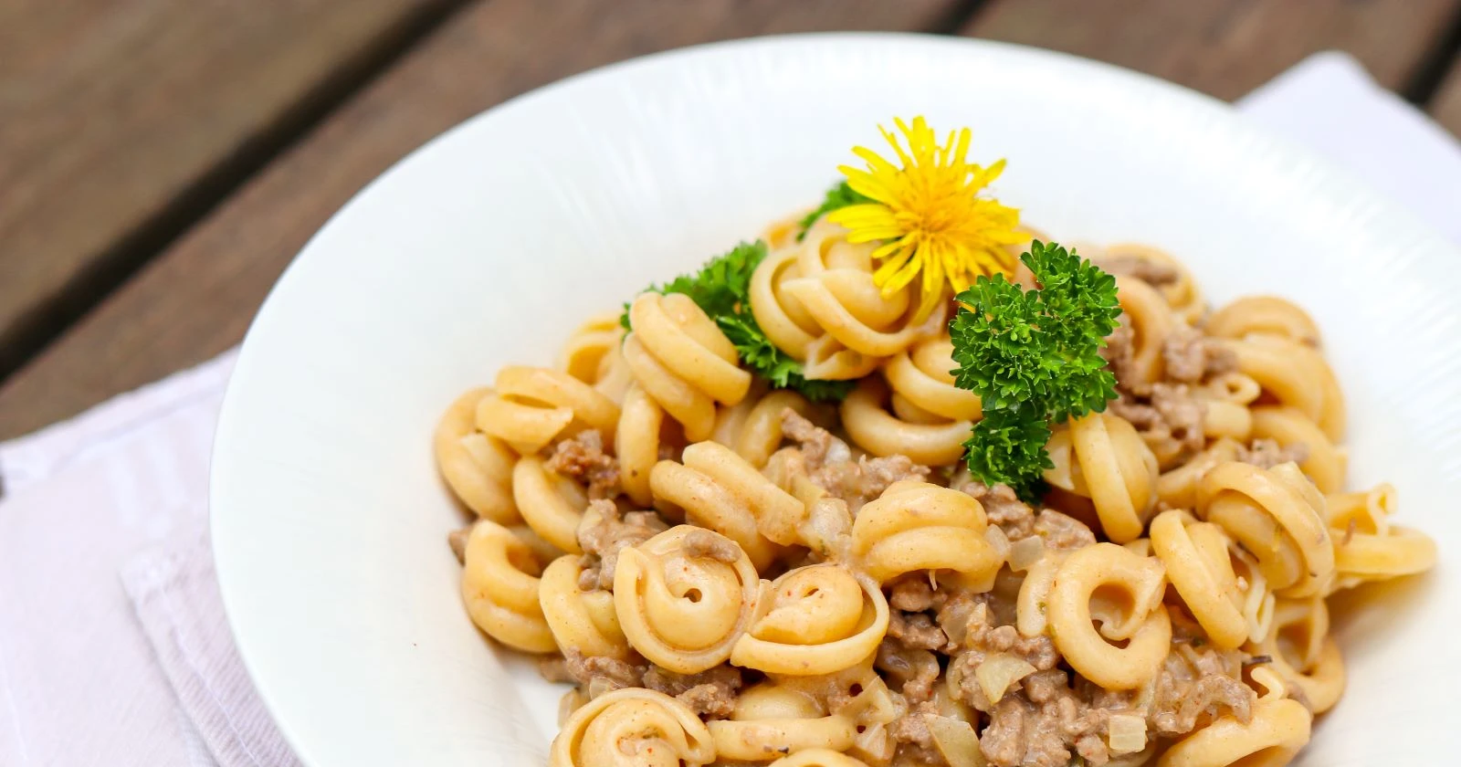 Jauhelihapasta valkoisella lautasella voikukalla koristeltuna.