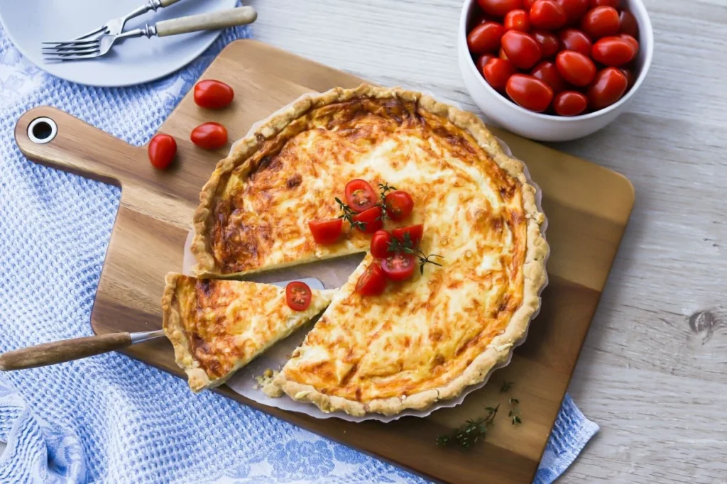 Juustopiirakka, joka on irrotettu vuoasta leivinpaperin avulla ja pieniä tomaatteja.