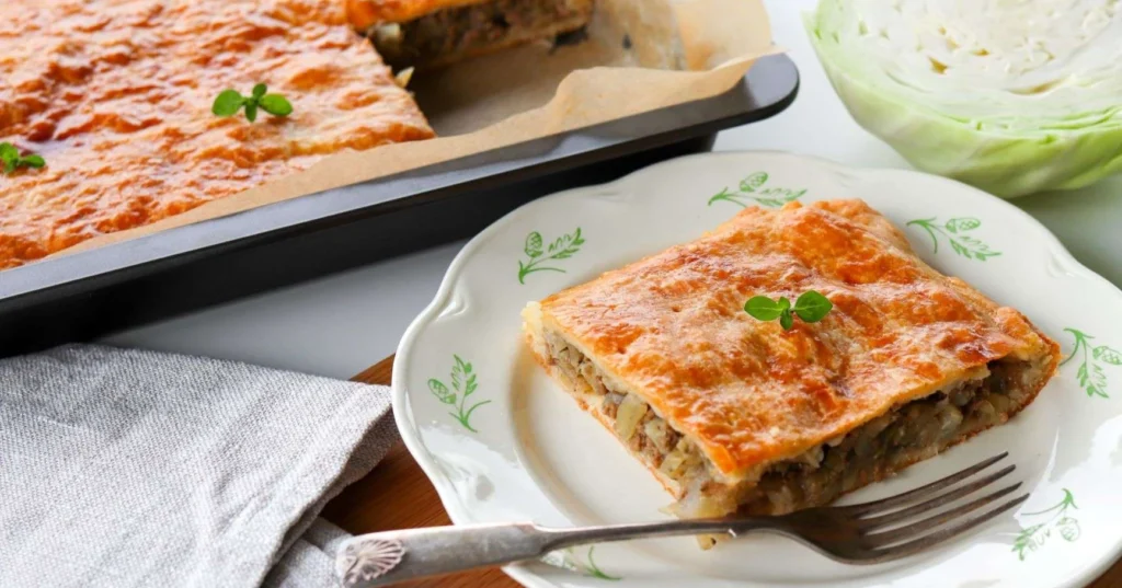 Pala kaalipiirakkaa lautasella ja taustalla pellillinen piirakkaa.