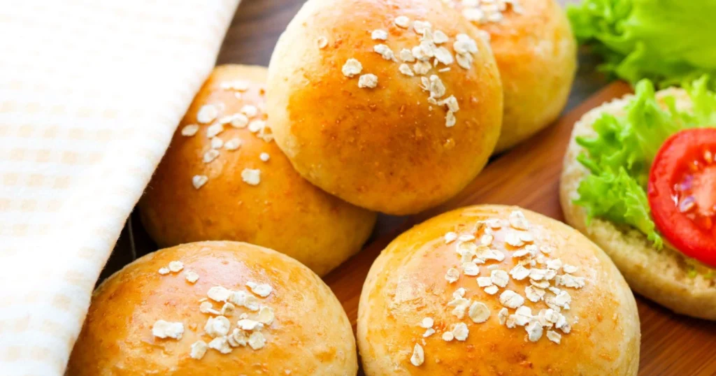 Tuoreet kaurasämpylät liinan alla sekä yksi halkaistuna.