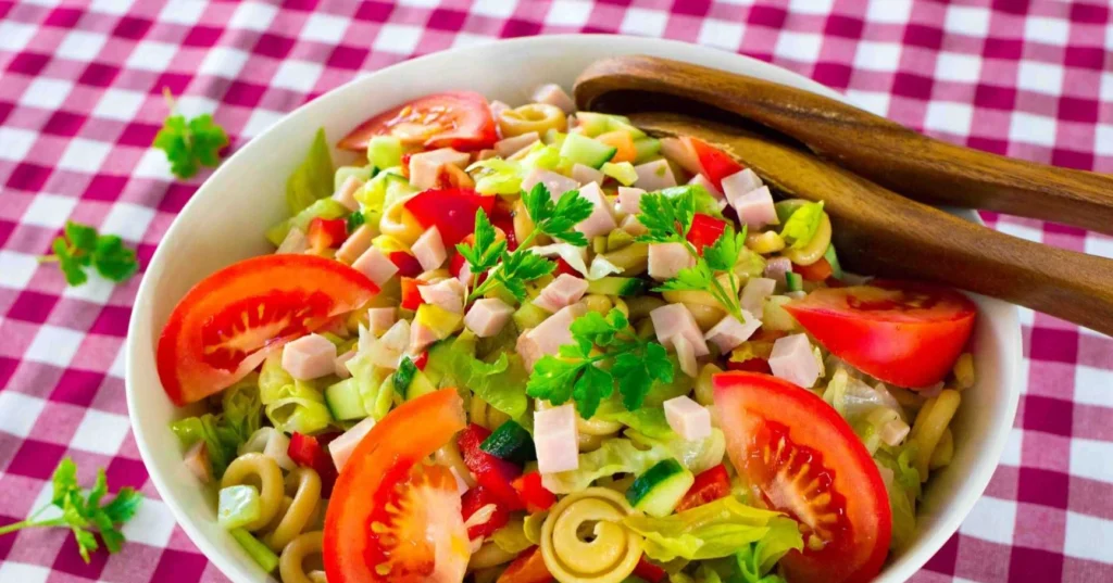 Värikäs kinkkusalaatti kulhossa puisten ottimien kera.