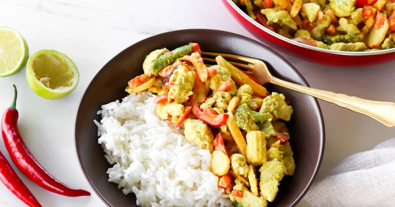 Kookoskana riisin kanssa lautasella sekä tuoretta chiliä ja limeä.