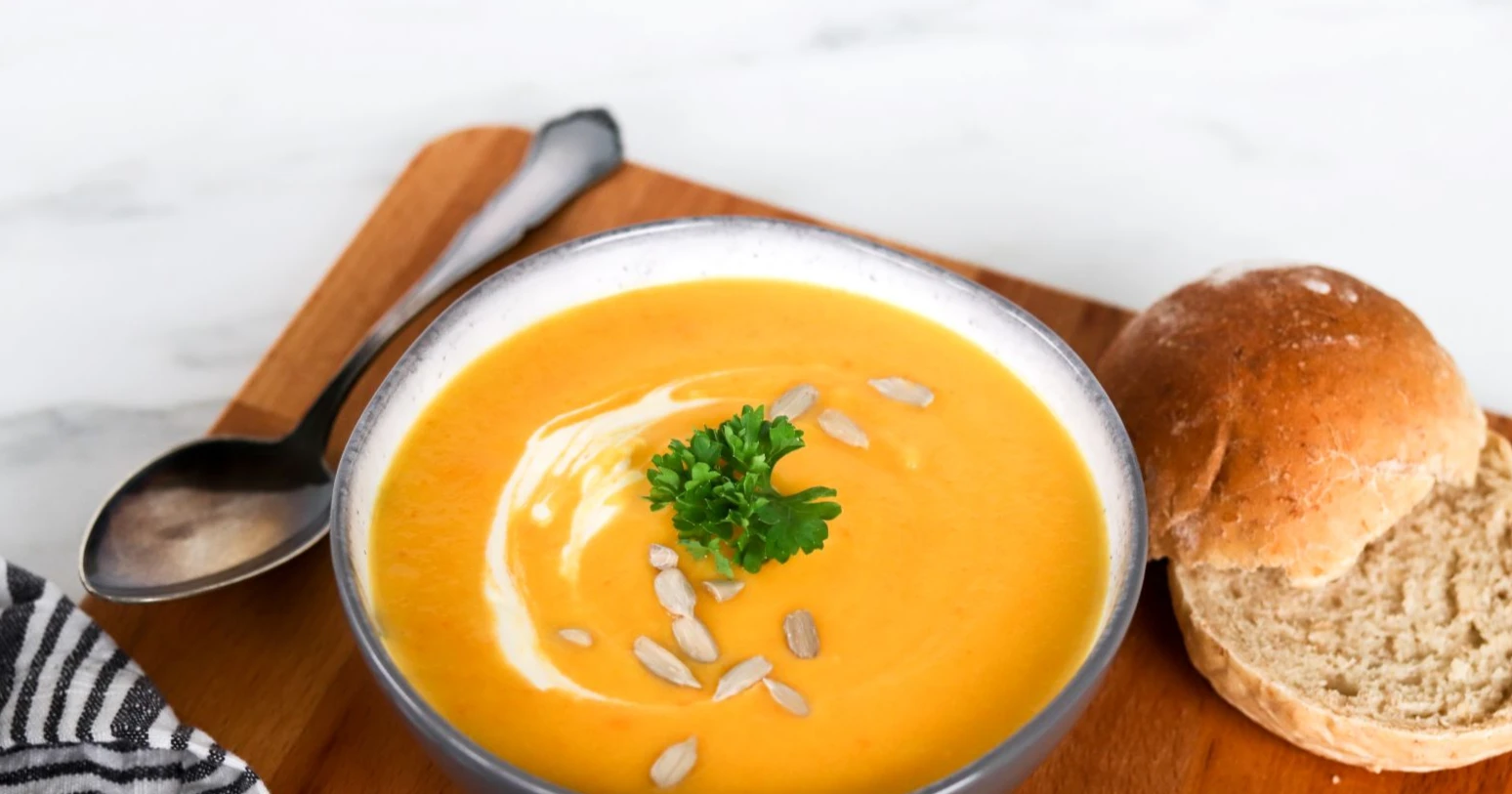 Kurpitsakeitto smetanalla koristeltuna sämpylän kera.