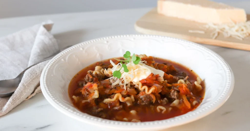 Lasagnekeitto valkoisella lautasella juustoraasteella höystettynä.