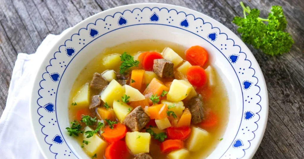 Värikäs lihakeitto syvällä sinivalkoisella lautasella.