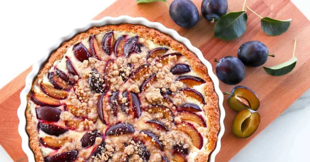 Luumupiirakka, jonka ympärillä on tuoreita tummia luumuja.