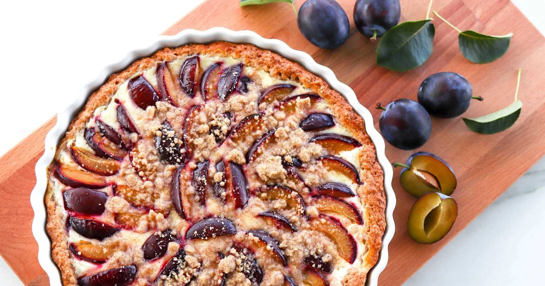 Luumupiirakka, jonka ympärillä on tuoreita tummia luumuja.