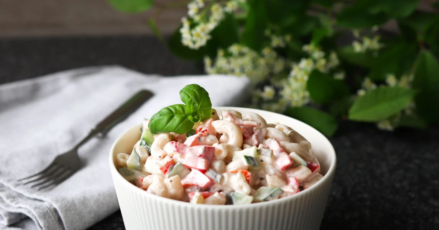 Makaronisalaatti tarjolla pienessä kulhossa, jonka taustalla on tuomen kukkia.
