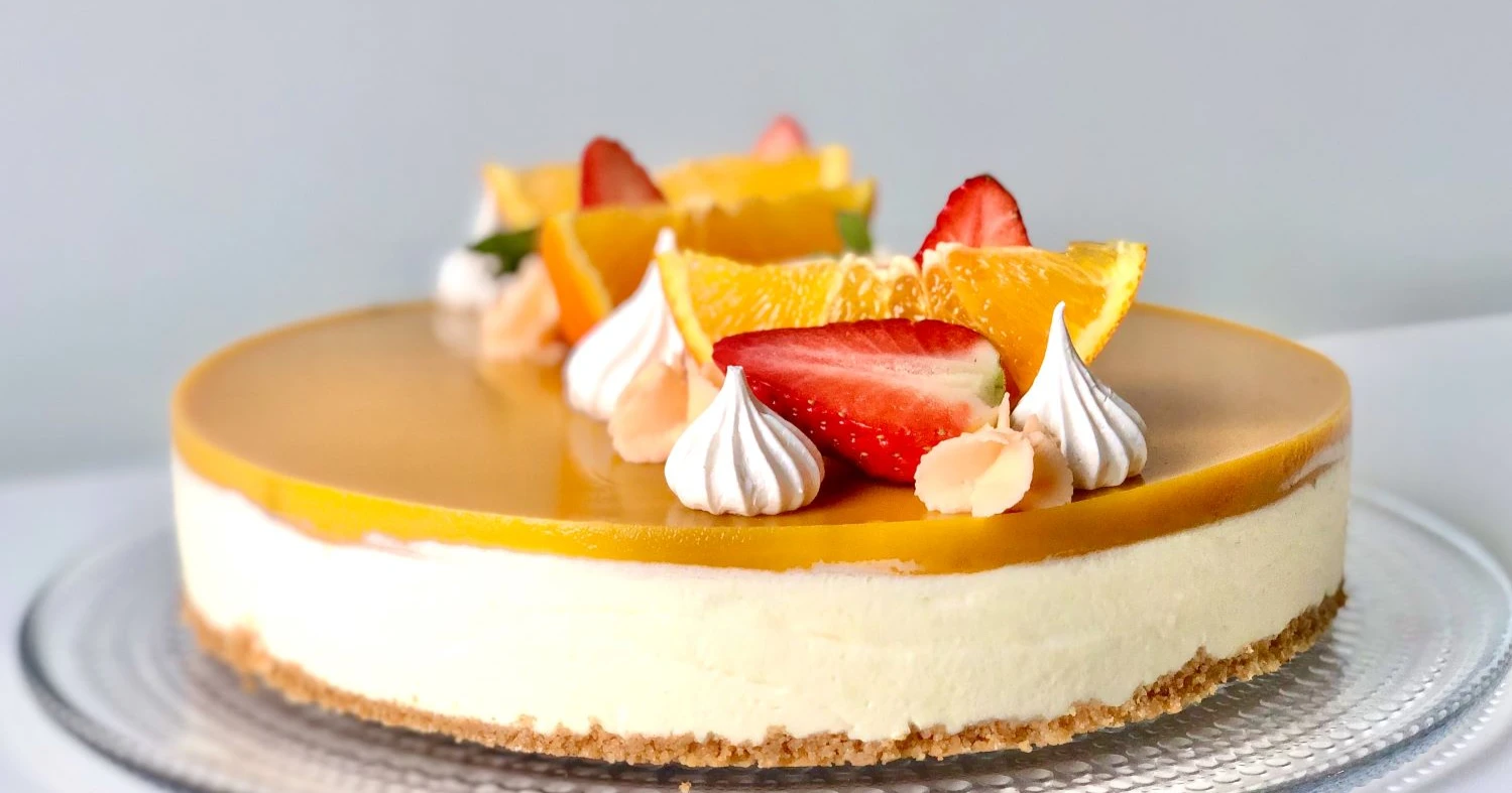 Mangojuustokakku kiilteellä ja tuoreilla hedelmillä koristeltuna.