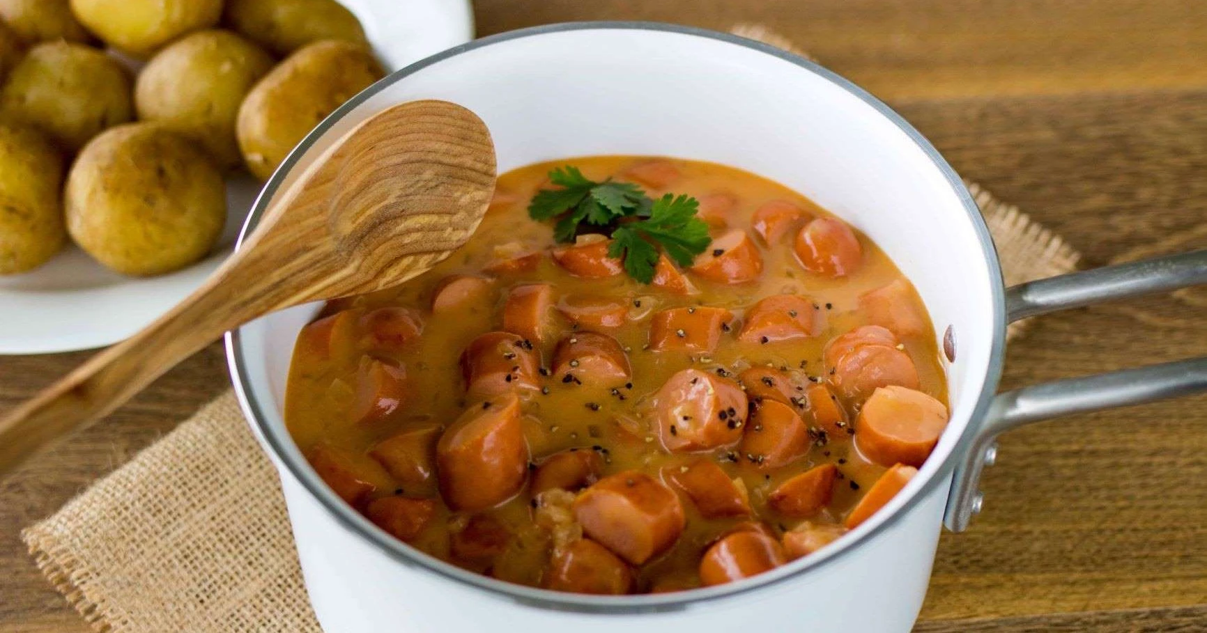 Nakkikastike pienessä valkoisessa kattilassa.