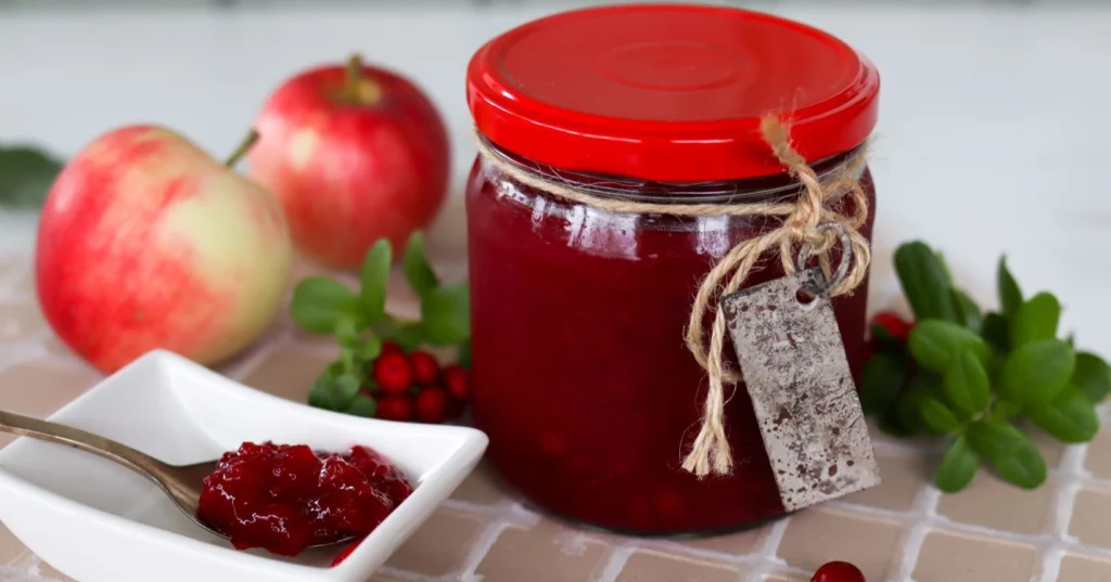 Omena-puolukkahillo lasipurkissa, jossa on punainen kansi.