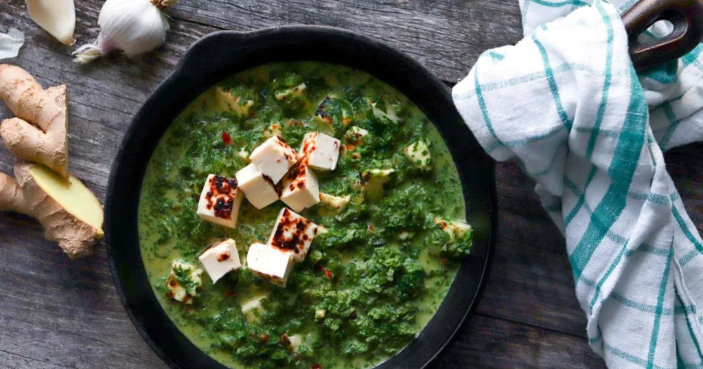 Palak paneer leipäjuustosta mustalla paistinpannulla.
