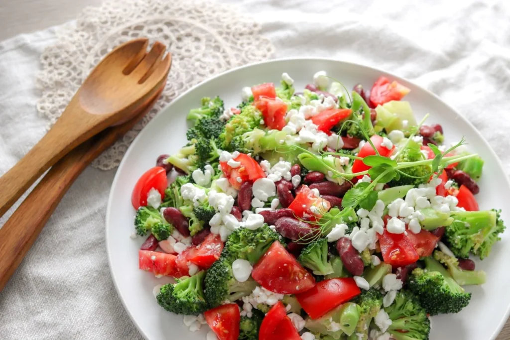 Papu-parsakaalisalaattia valkoisella tarjoilulautasella puisten salaattiottimien vieressä.