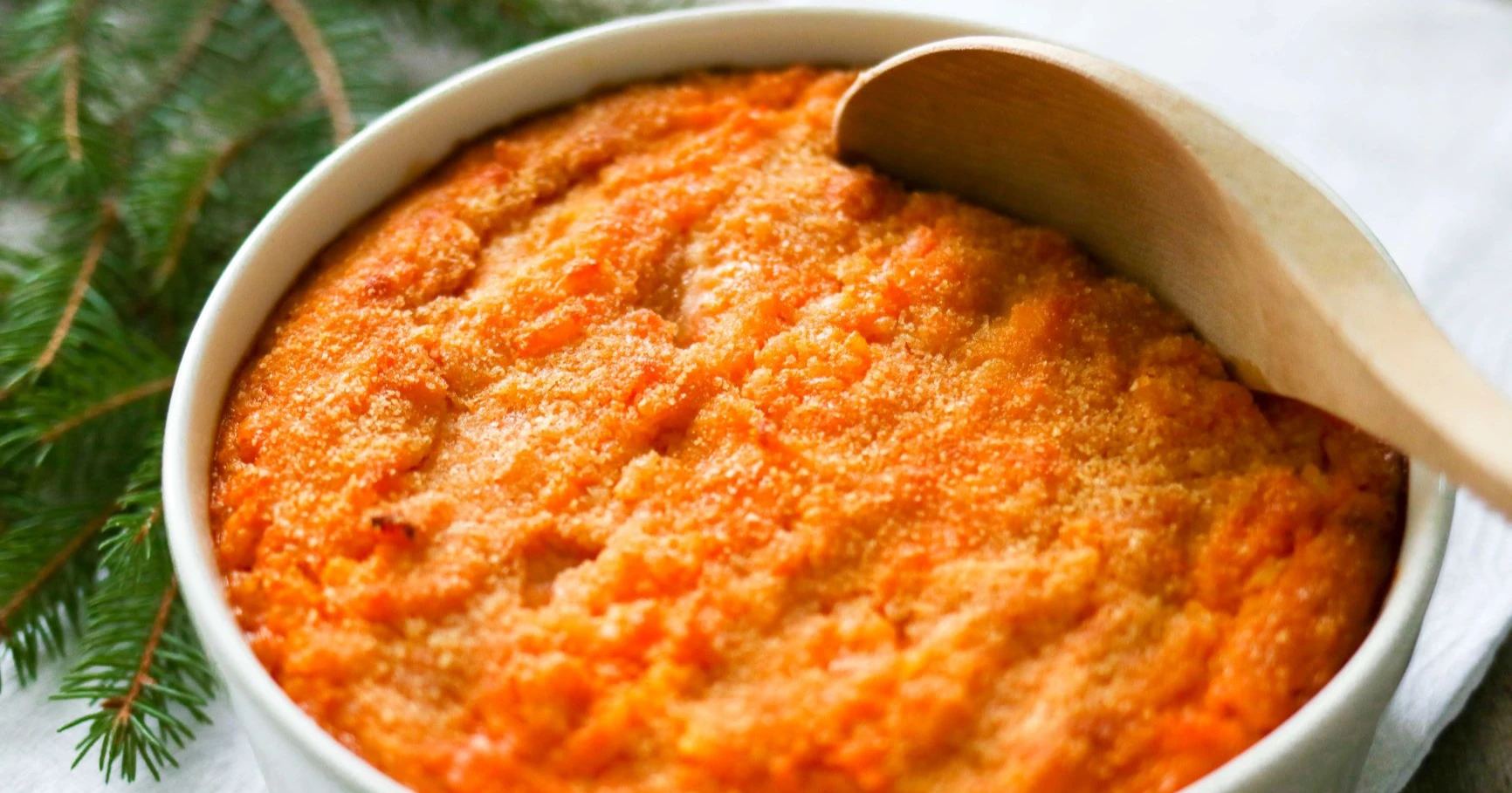 Porkkanalaatikko perinteisen puukauhan kanssa valkoisessa uunivuoassa.