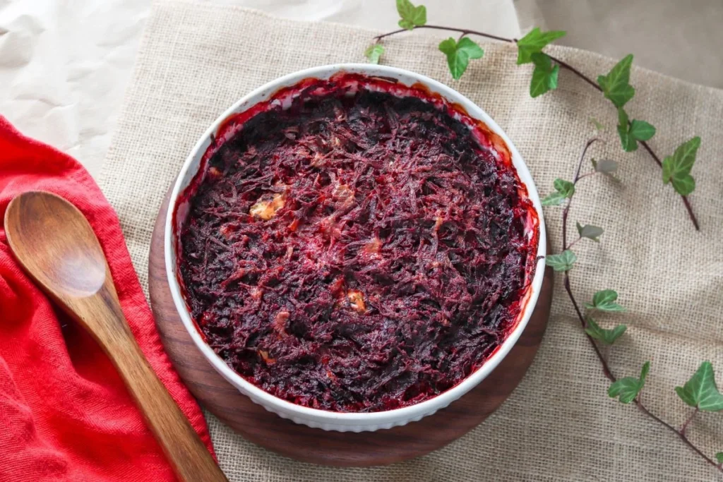 Aura-punajuurilaatikko paistamisen jälkeen, vieressä puukauha punaisen liinan päällä.