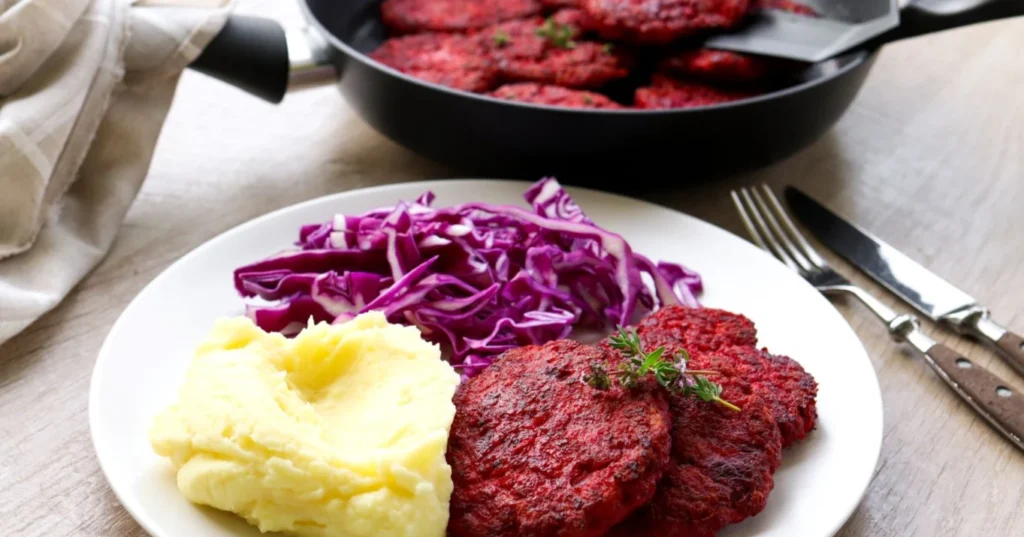 Punajuuripihvit lautasella itse tehdyn muusin ja violetin kaalisalaatin kanssa.