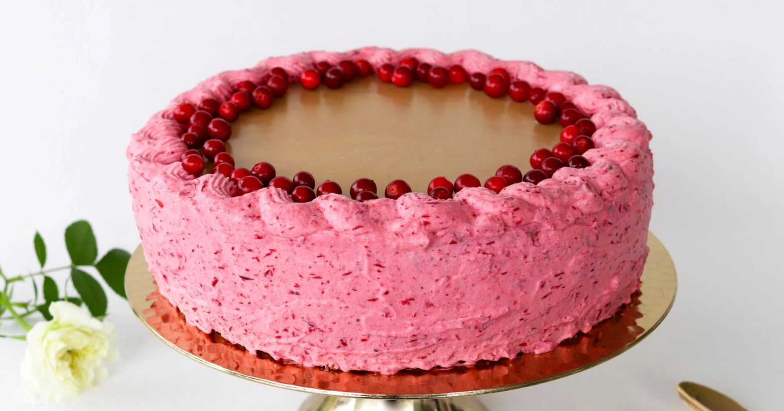 Kinuskipäällysteinen puolukkakakku, jonka reunoilla on vaaleanpunaista kuorrutusta.