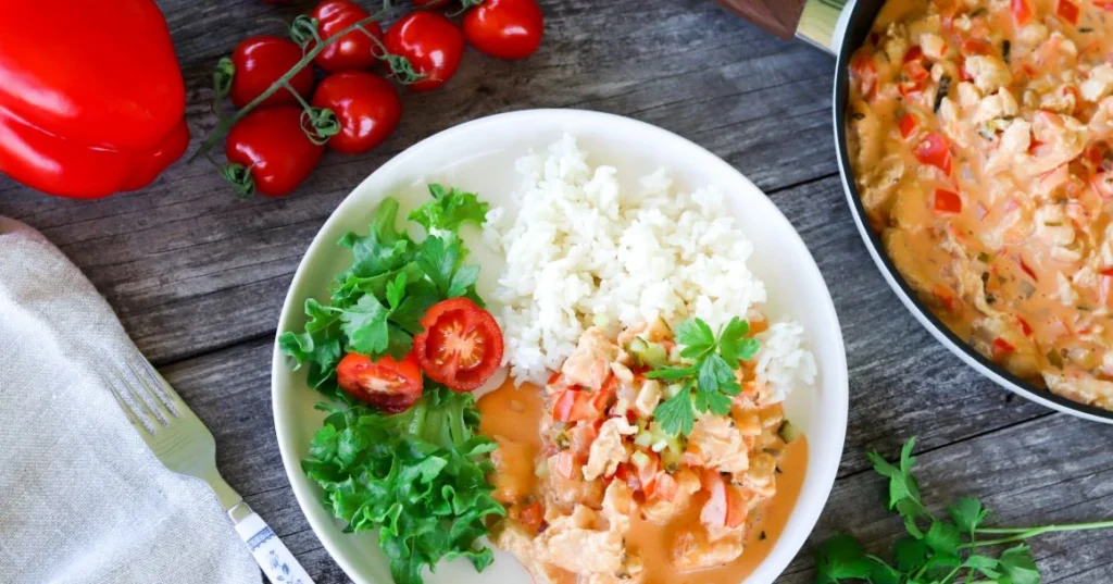 Smetanakanaa valkoisella lautasella riisin ja raikkaan salaatin kanssa.