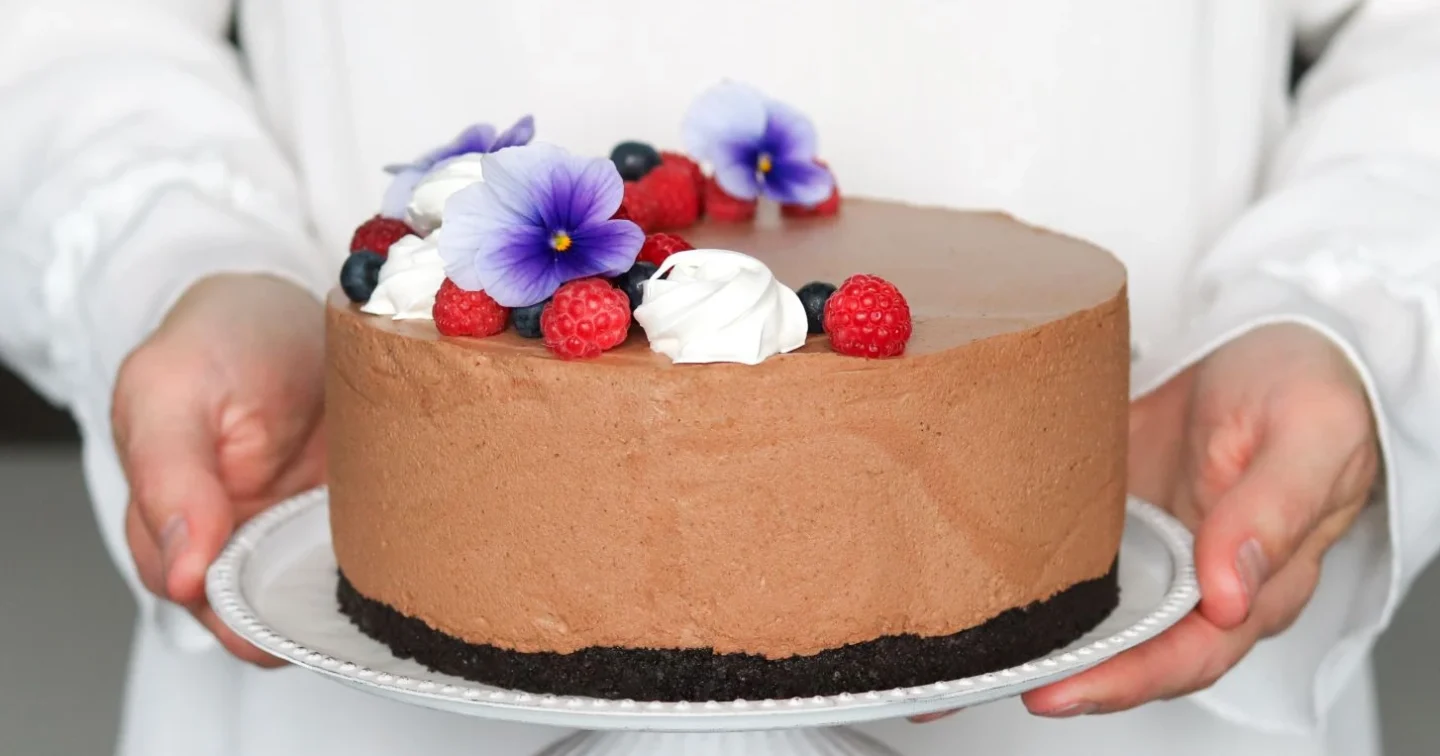 Suklaajuustokakku vadelmilla ja kukilla koristeltuna.