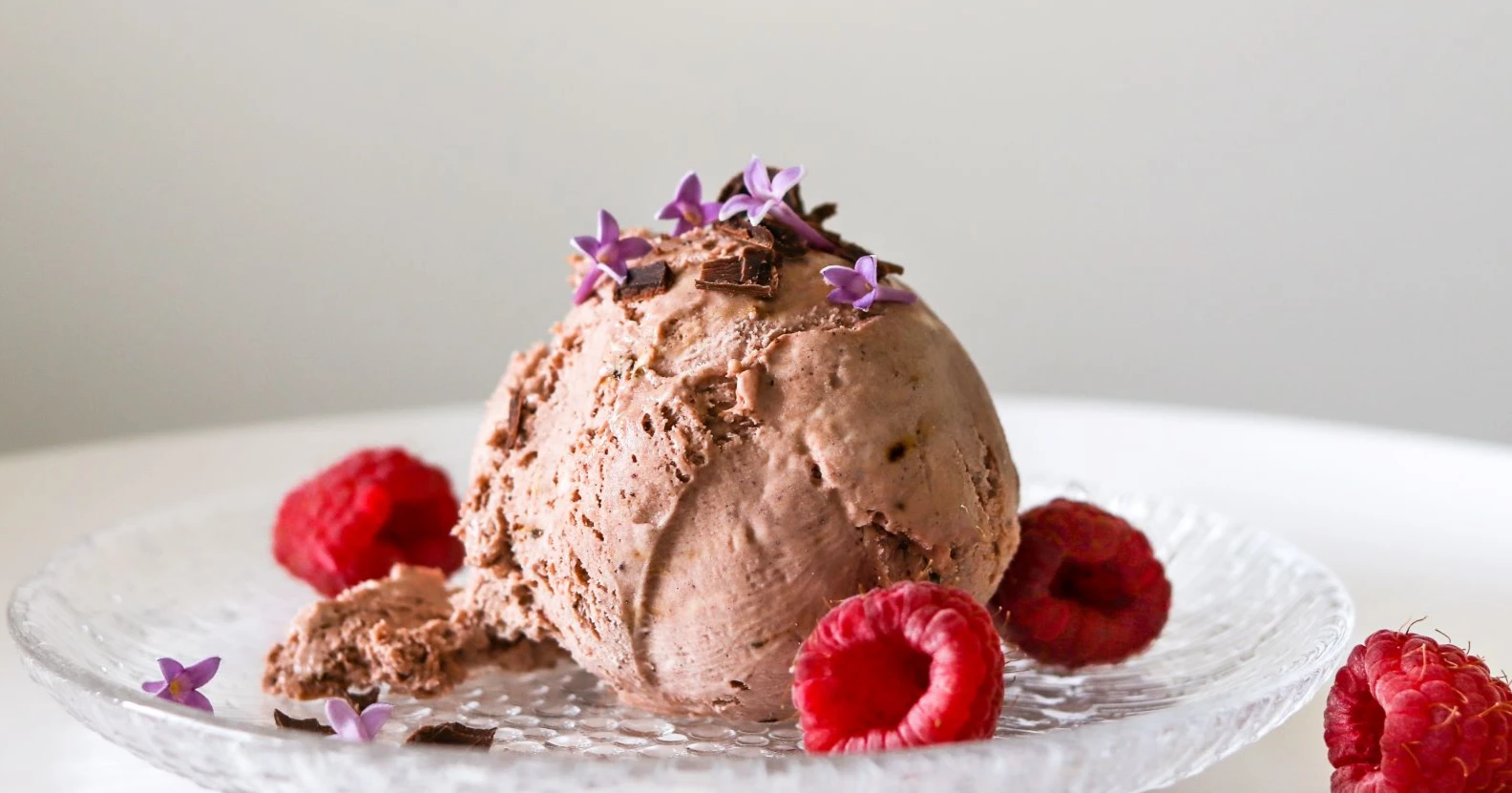 Vegaaninen suklaajäätelö lasilautasella vadelmilla koristeltuna.